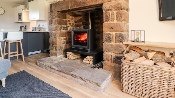 A stone fireplace with a TV, a kitchen area, and a bar stool. - Moss Side Retreat (Skipton)
