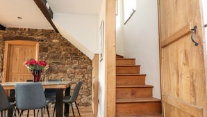 A dining area with a stone wall, wooden staircase, and a wooden door. - Moss Side Retreat (Skipton)