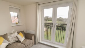 A living room with a beige sofa, a radiator, and a sliding glass door leading to a balcony with a view of greenery. - Valley View (Whitby)