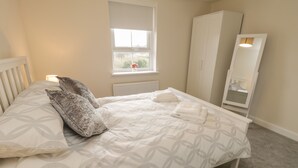 A bedroom with a bed, pillows, a window, a radiator, a wardrobe, and a mirror. - Valley View (Whitby)