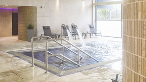 Een wellnessruimte met een bubbelbad, lounge stoelen en een betegelde vloer.