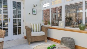 A cozy room with a wicker sofa, a round wooden coffee table with decorative items, and a large window with a view of trees. - 40 Bowmont Court (Kelso)
