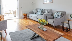 A modern living room with a grey sofa, a wooden coffee table, and a vase of sunflowers. - 40 Bowmont Court (Kelso)