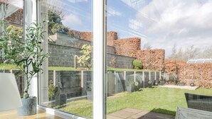 A view through a window of a garden with a wooden bench, a potted plant, and a stone wall. - 40 Bowmont Court (Kelso)