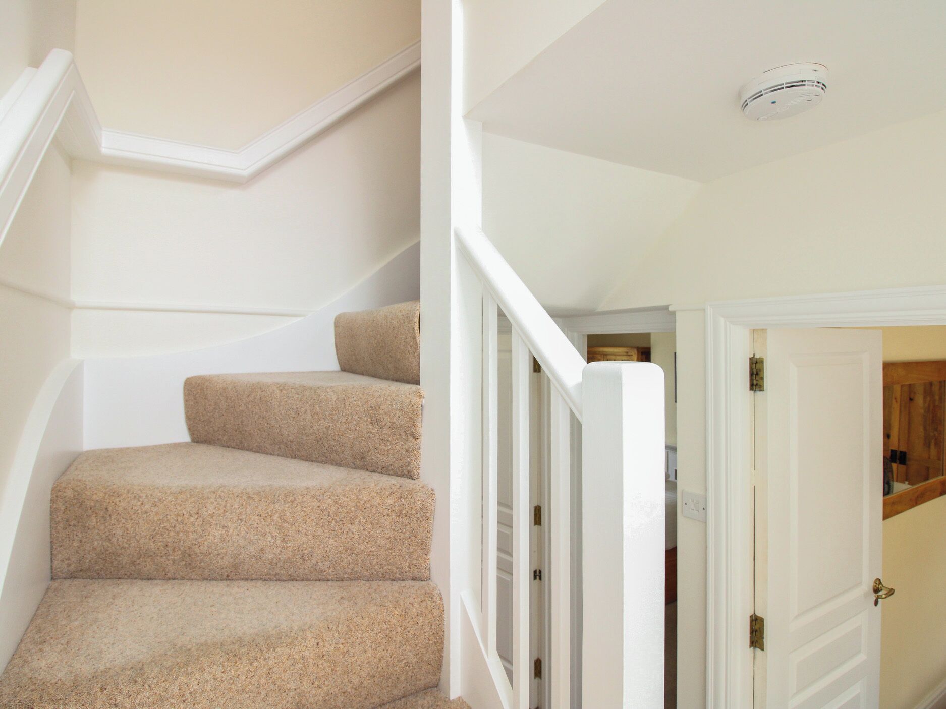 A staircase with carpeted steps, white railings, and a door leading to another room.