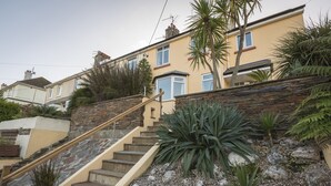 A residential building with a stone staircase leading to a door, surrounded by various plants and a rocky garden. - Home (Salcombe)