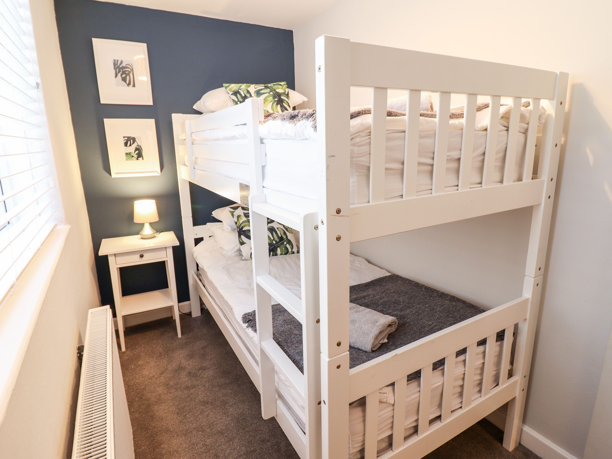 A bunk bed room with a nightstand, a lamp, and framed pictures on the wall.