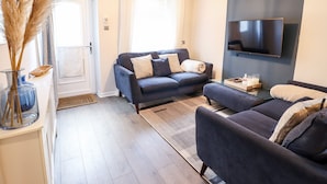 A modern living room with a dark blue sofa, a glass coffee table, and a flat-screen TV mounted on the wall. - Driftwood Terrace (Porthmadog)