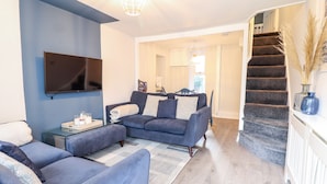 A modern living room with a blue sofa, a coffee table, and a flat-screen TV mounted on the wall. - Driftwood Terrace (Porthmadog)