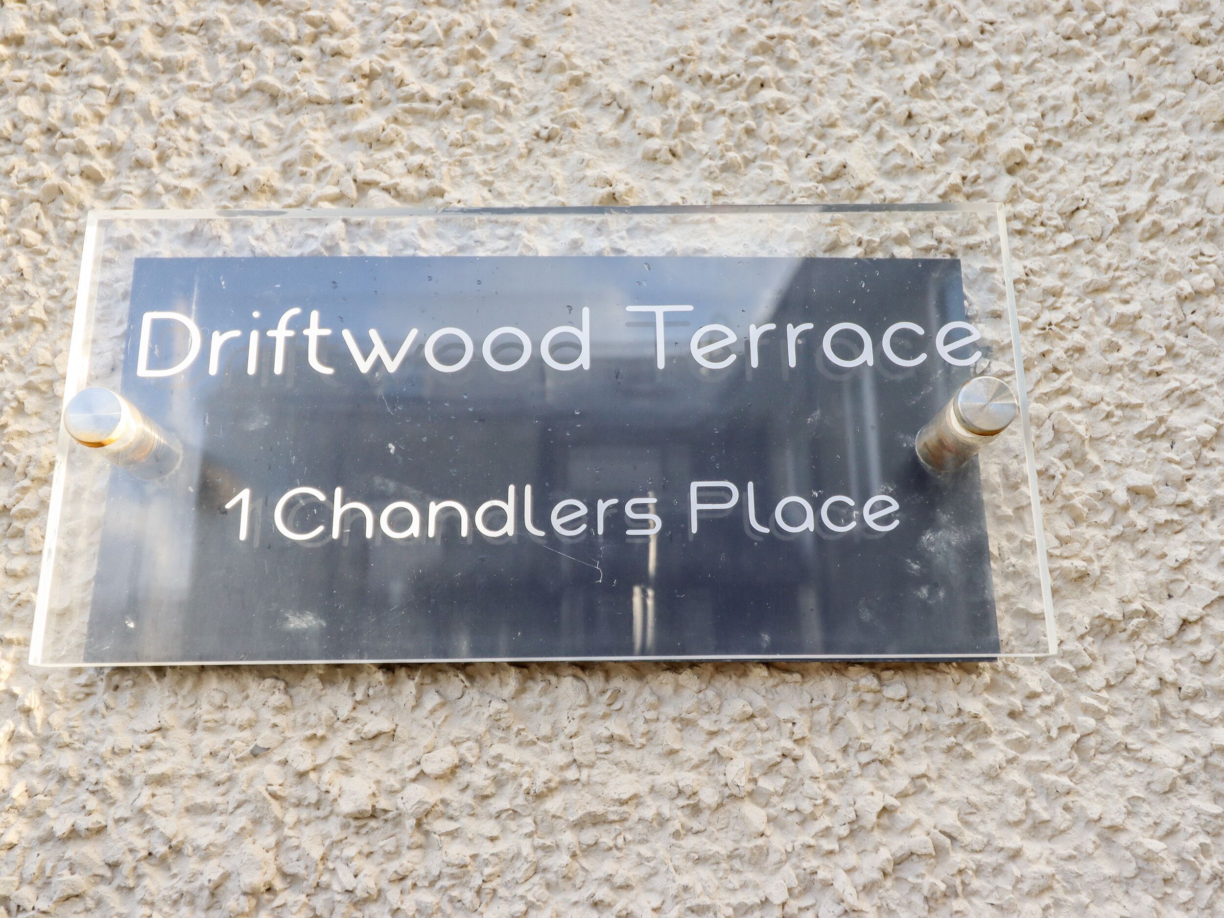 A sign with the text "Driftwood Terrace 1 Chandlers Place" mounted on a textured wall.