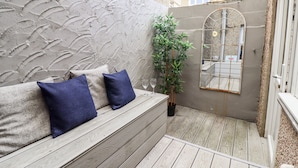 A wooden deck with a bench and cushions, a potted plant, and a mirror on the wall. - Driftwood Terrace (Porthmadog)