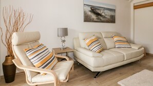 A living room with a sofa, a chair, a lamp, a painting, and a vase with branches. - Westfields (Launceston)