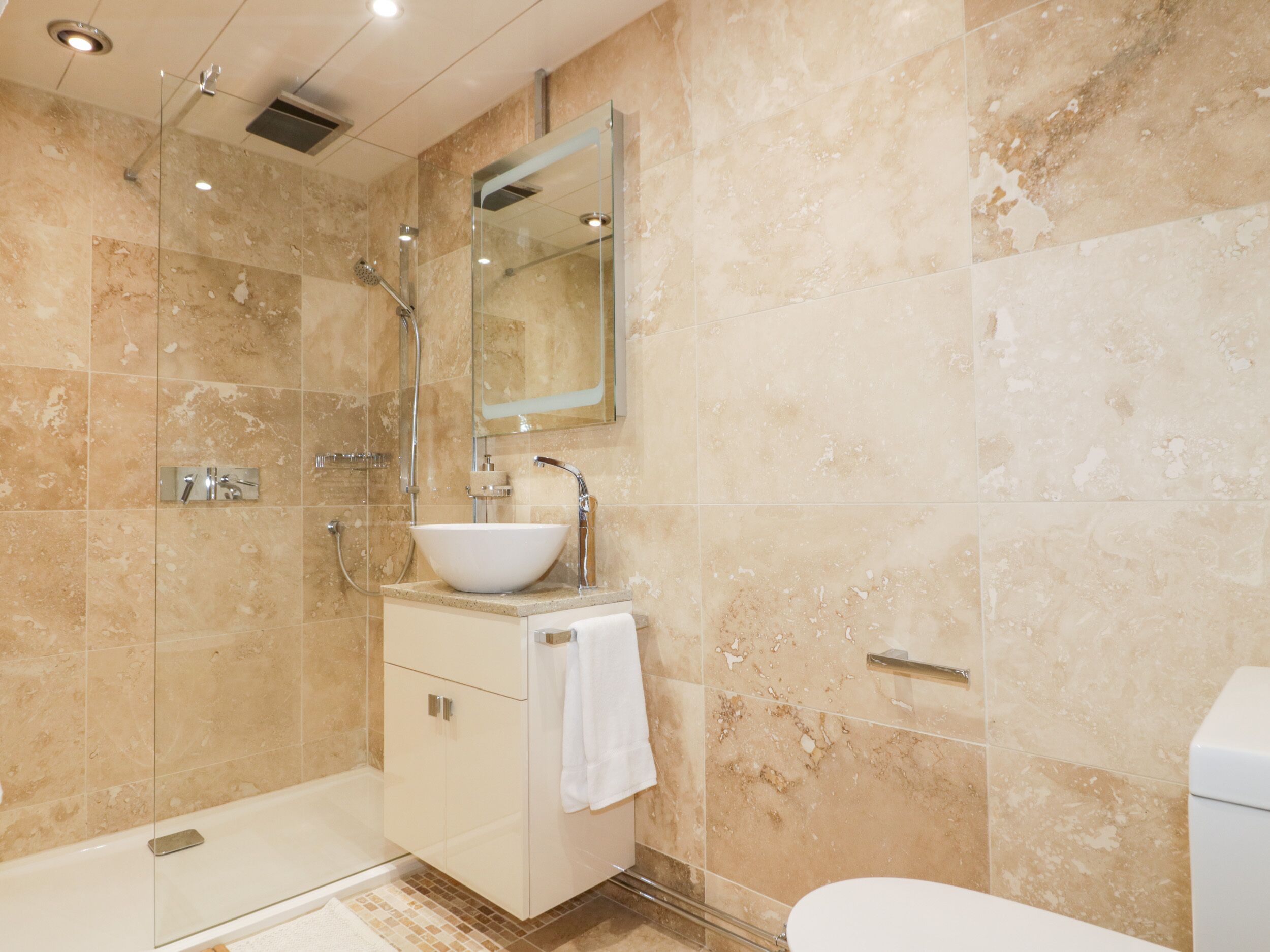 Un baño moderno con ducha de vidrio, un lavamanos blanco y un inodoro.