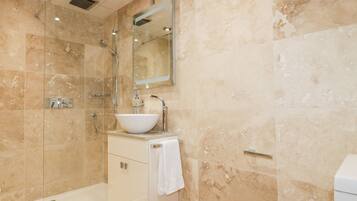 Un baño moderno con ducha de vidrio, un lavamanos blanco y un inodoro.