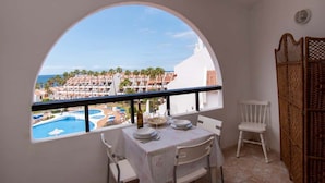 A balcony with a view of a pool and buildings, a table set with plates and a bottle, and a chair. - Parque Santiago II 269 - Studio with sea and pool (Playa de la Américas)