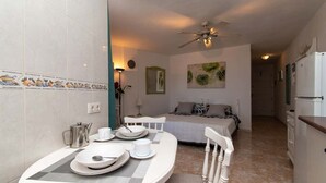 A compact hotel room with a dining area, a bed, a kitchenette, and a ceiling fan. - Parque Santiago II 269 - Studio with sea and pool (Playa de la Américas)
