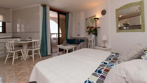 A hotel room with a bed, a desk, a chair, a sofa, a small table, a lamp, and a mirror. - Parque Santiago II 269 - Studio with sea and pool (Playa de la Américas)