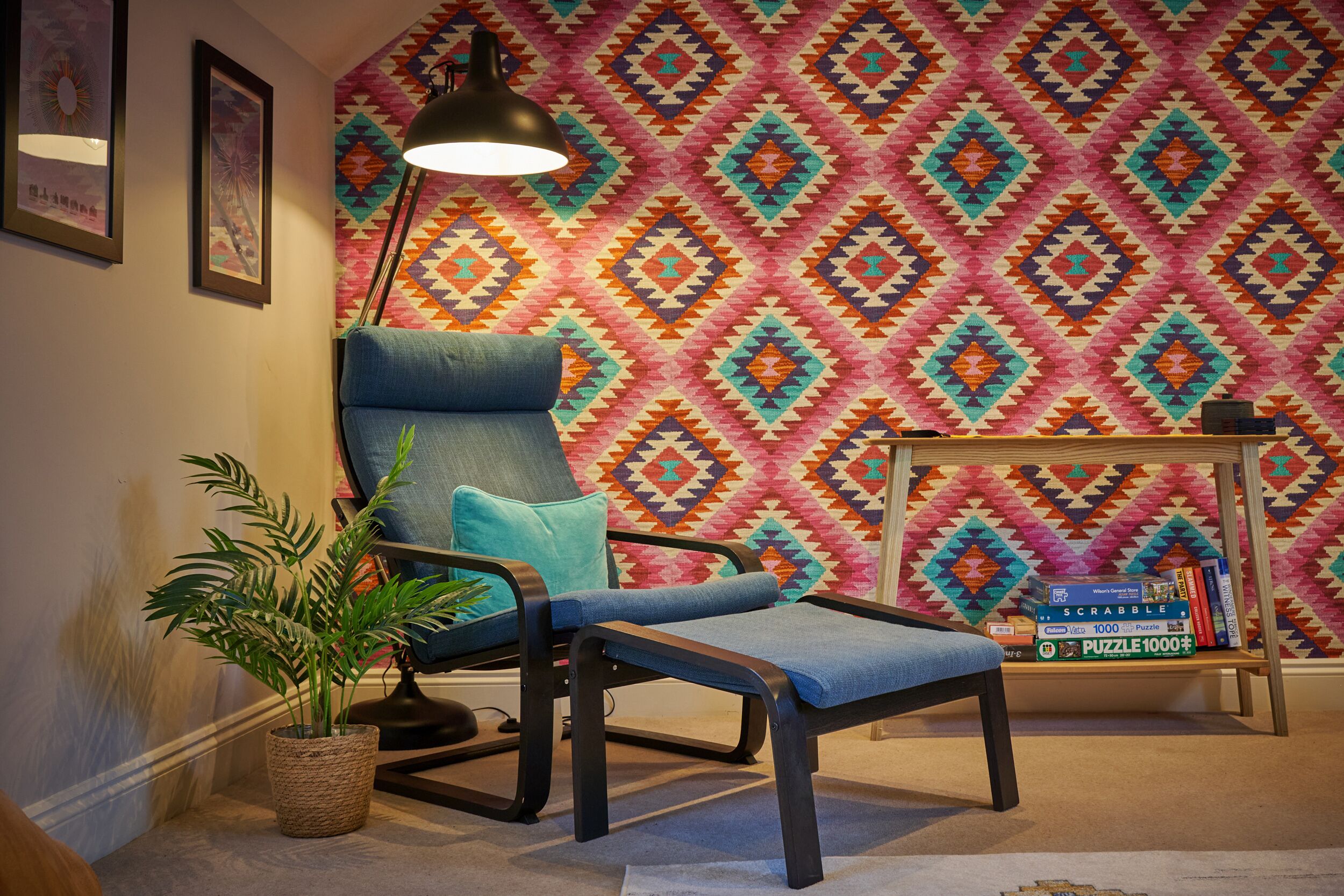 A room with a patterned wall, a blue armchair, a small table with books, and a floor lamp.