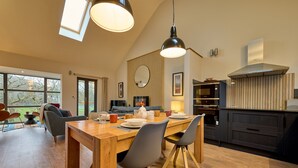 A modern kitchen with a wooden dining table, grey chairs, and a large window. - Riverside Park 5 (Keswick)