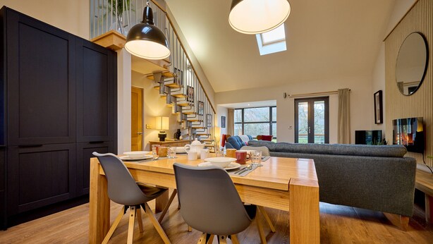 A modern kitchen with a dining table, chairs, and a staircase leading to a loft area. - Riverside Park 5 (Keswick)