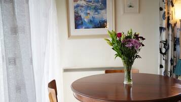 Ein runder Holztisch mit einer klaren Glasvase, die Blumen enthält, umgeben von Holzstühlen mit blauen Kissen.