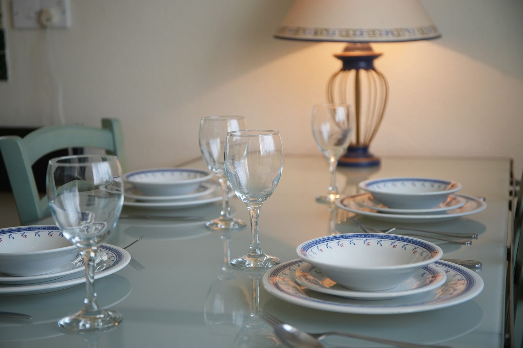 A dining table with plates, glasses, and cutlery, a lamp, and a chair.