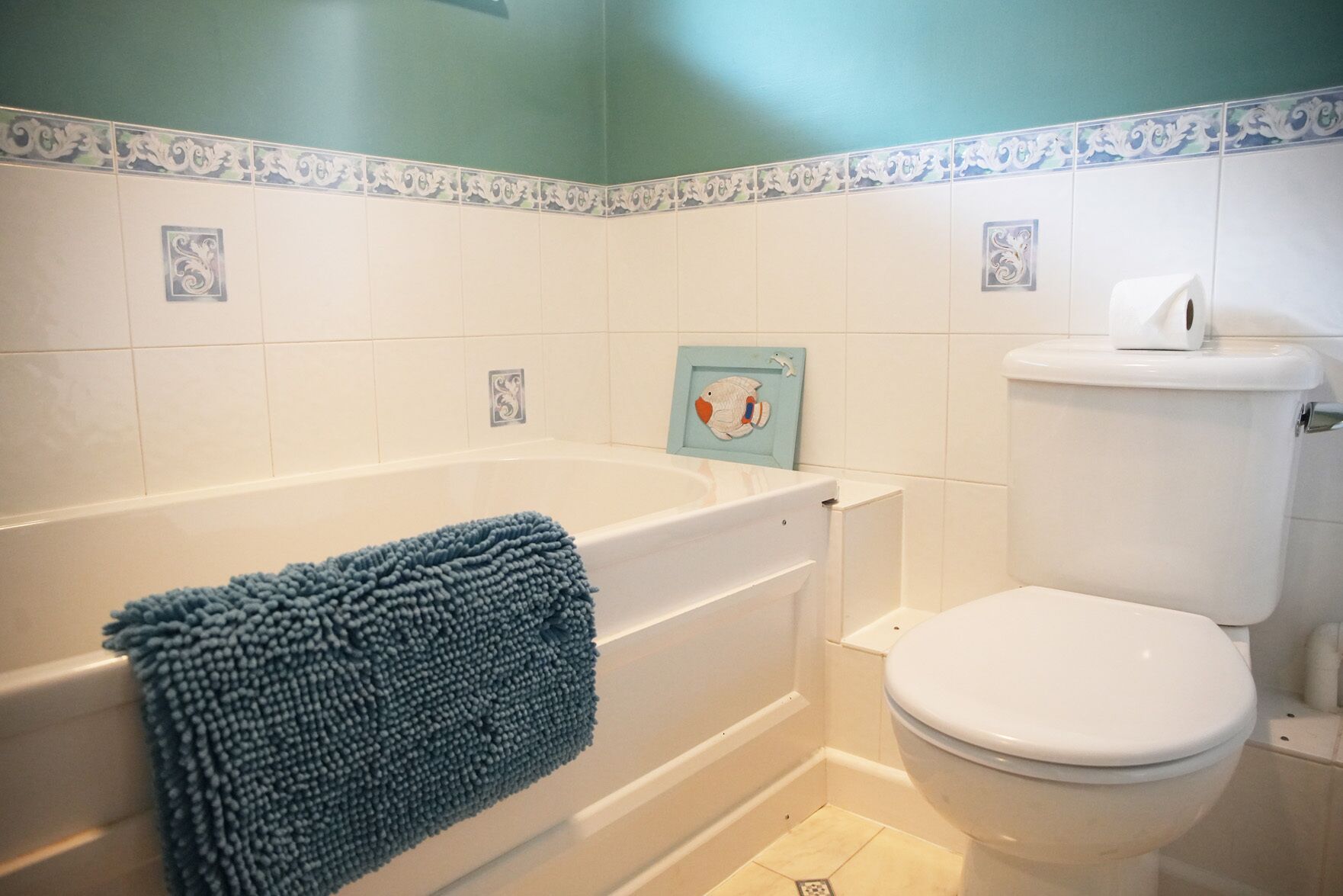 A bathroom with a bathtub, toilet, and decorative tiles.