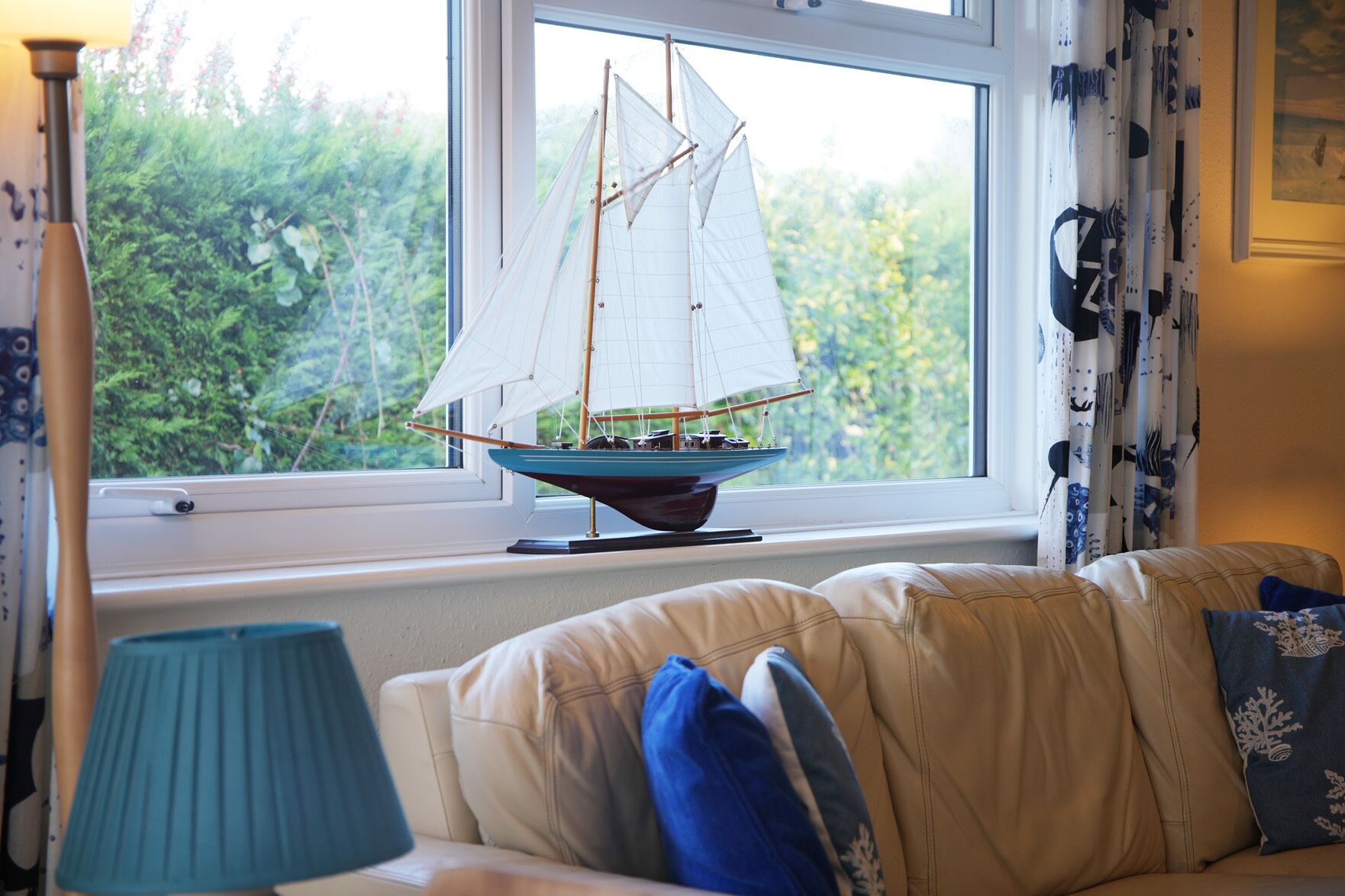 En modellsegelbåt på en fönsterbräda, en lampa och en soffa med kuddar.