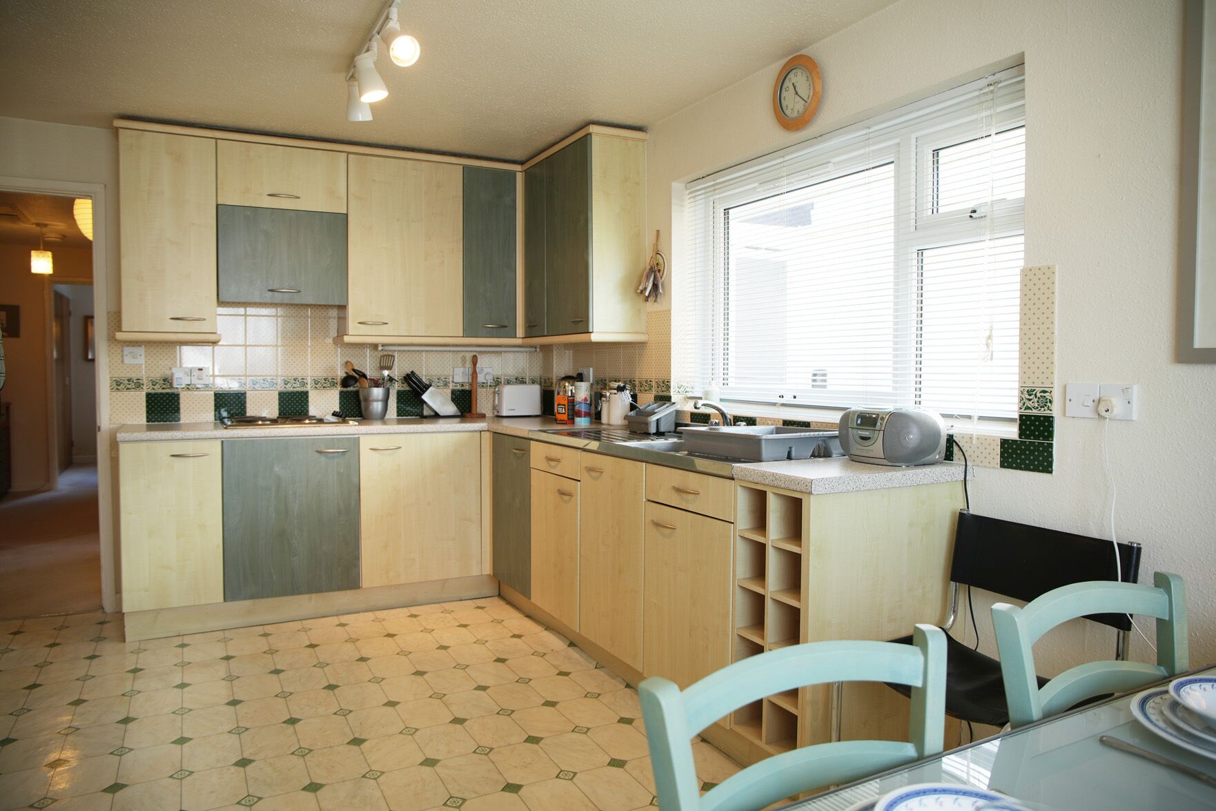 Una cocina con armarios de madera clara, piso de baldosas y un comedor con mesa y sillas.