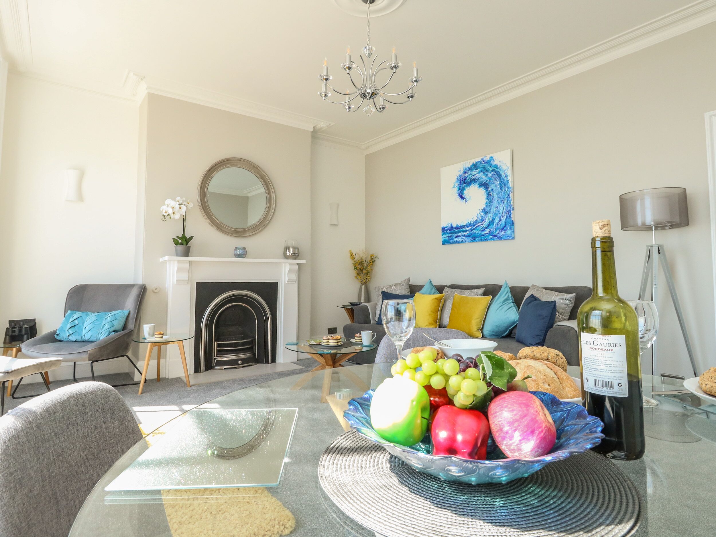 A living room with a fireplace, a sofa, a coffee table with fruit, and a bottle of wine.