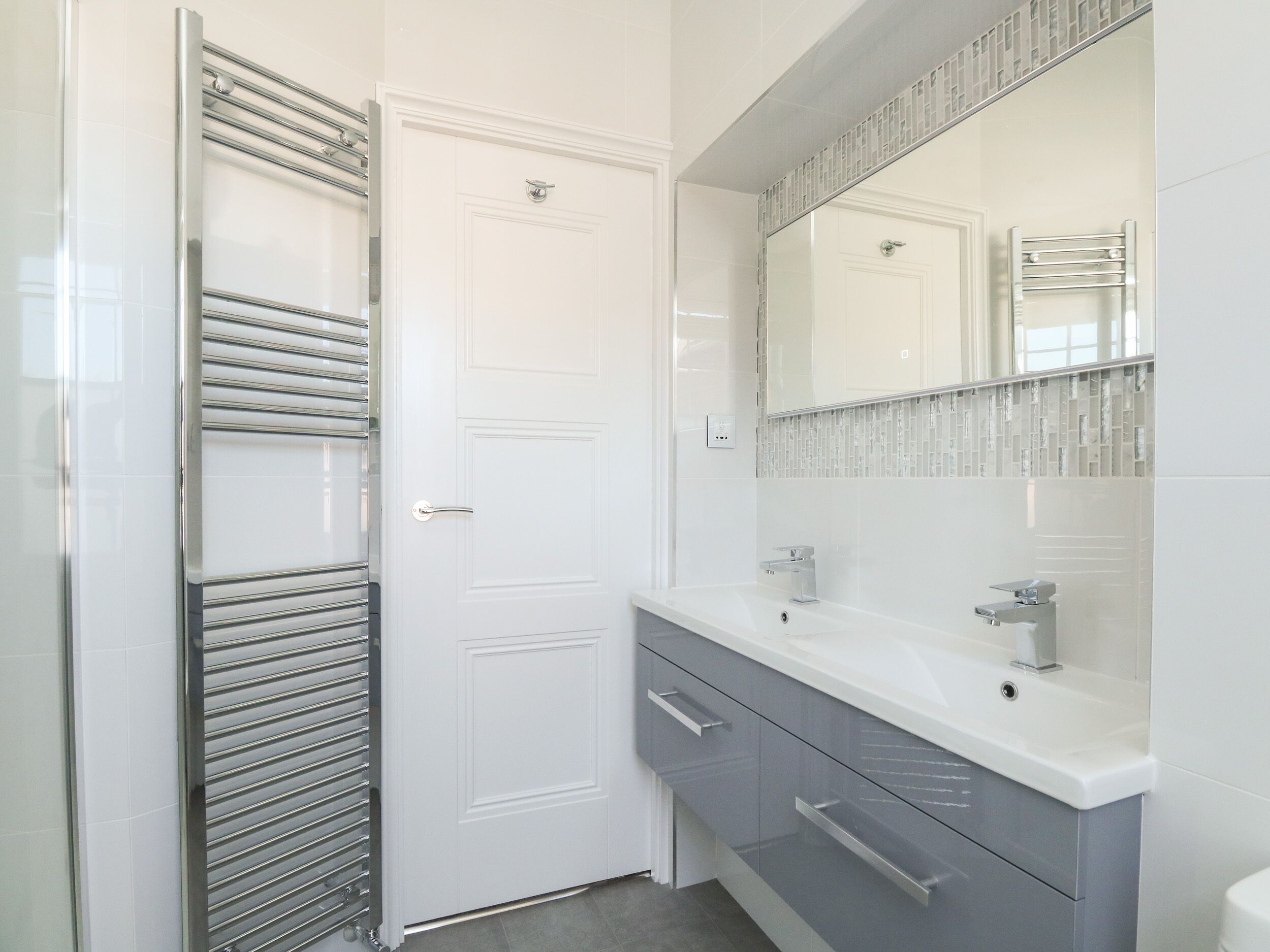 A modern bathroom with a white door, a glass shower enclosure, a vanity with a mirror, and a towel rack.
