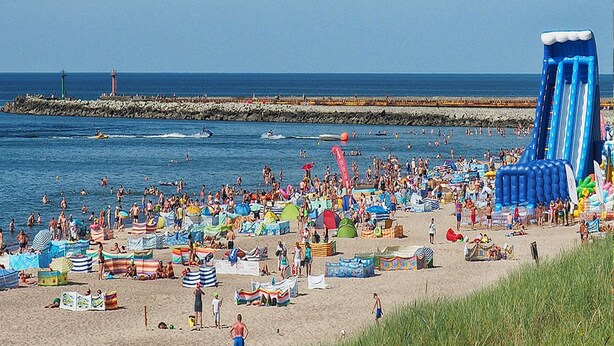 A crowded beach with inflatable slides and a lighthouse in the background. - Serene Bungalow in Darłowo with Large Garden (Darłowo)