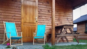 A wooden cabin with a door, two blue chairs, and a picnic table. - Serene Bungalow in Darłowo with Large Garden (Darłowo)