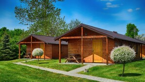 A wooden cabin with a covered porch, a picnic table, and a small tree in front. - Serene Bungalow in Darłowo with Large Garden (Darłowo)