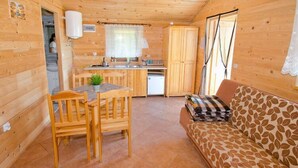 A wooden cabin with a kitchen, dining area, and a sofa. - Serene Bungalow in Darłowo with Large Garden (Darłowo)
