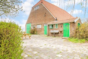 A brick building with a sloped roof, a green door, and a small outdoor seating area with a table and benches.
