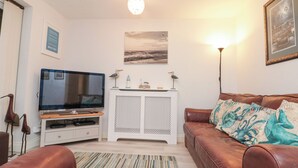 Ein Wohnzimmer mit einem braunen Ledersofa, einem Flachbildfernseher, einem weißen Schrank und einem gerahmten Bild an der Wand.