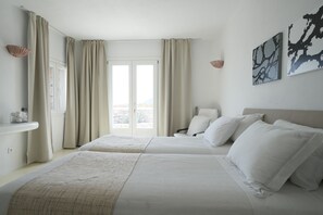 Two single beds with white bedding, a large window, and wall-mounted sconces.