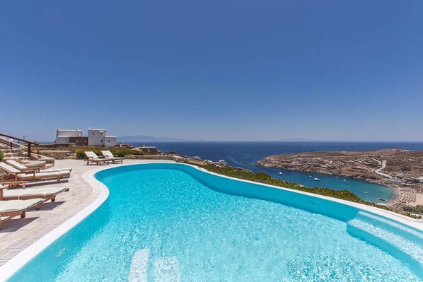 Relax by the pool with a view of the sea and distant land, surrounded by lounge chairs and a sleek building.