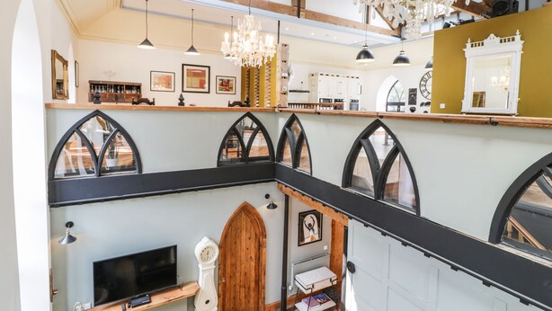 A spacious loft with high ceilings, exposed wooden beams, and a large chandelier. - Greystones Chapel (Caernarfon)