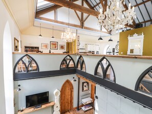 A spacious loft with high ceilings, exposed wooden beams, and a large chandelier. - Greystones Chapel (Caernarfon)