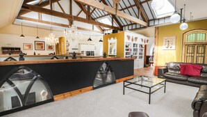 A spacious loft with a high ceiling, exposed wooden beams, a central bar area, and a cozy seating area with a leather sofa. - Greystones Chapel (Caernarfon)