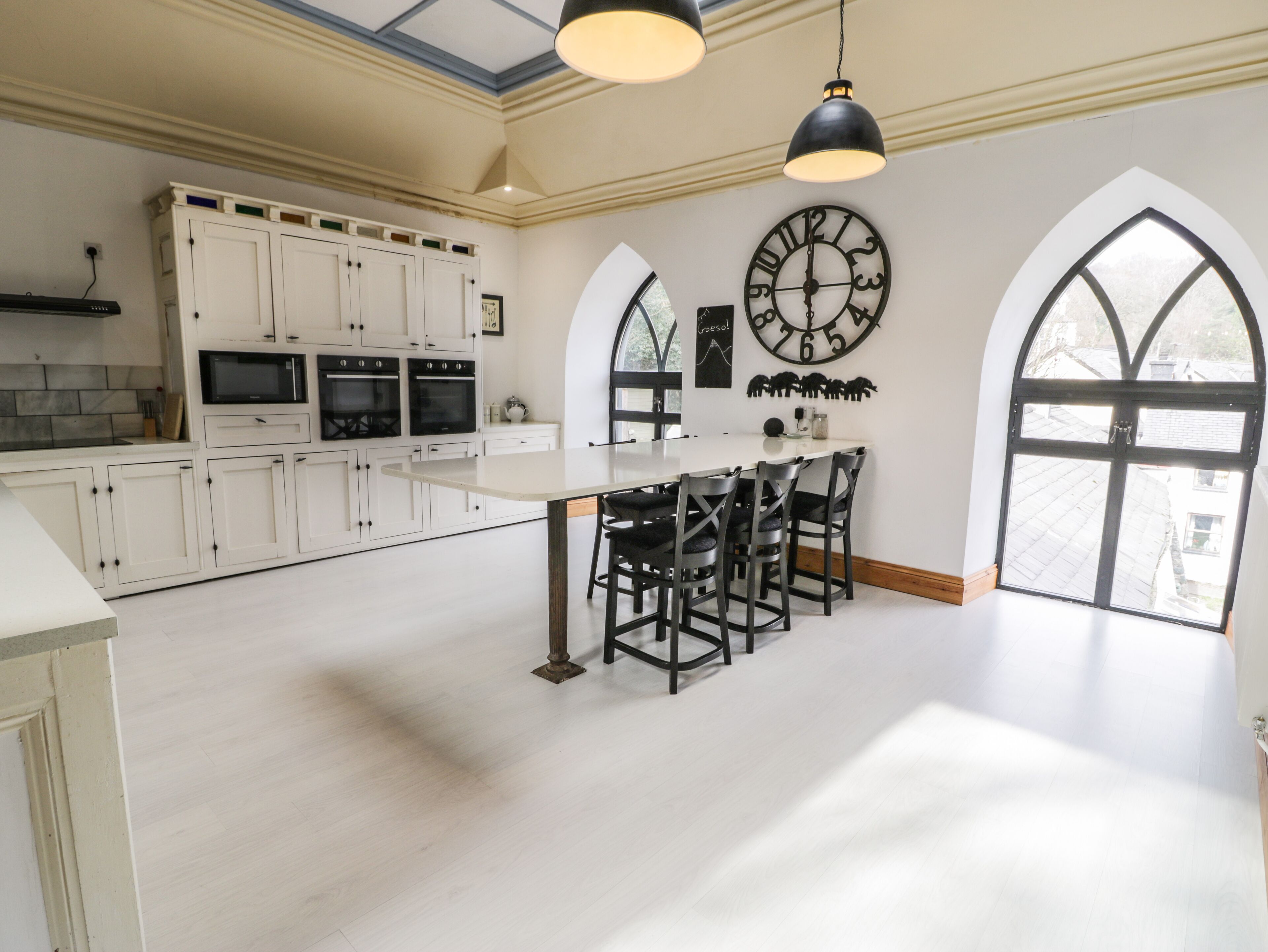 Un'ampia cucina con mobili bianchi, un'isola centrale con sgabelli da bar e un grande orologio a parete.