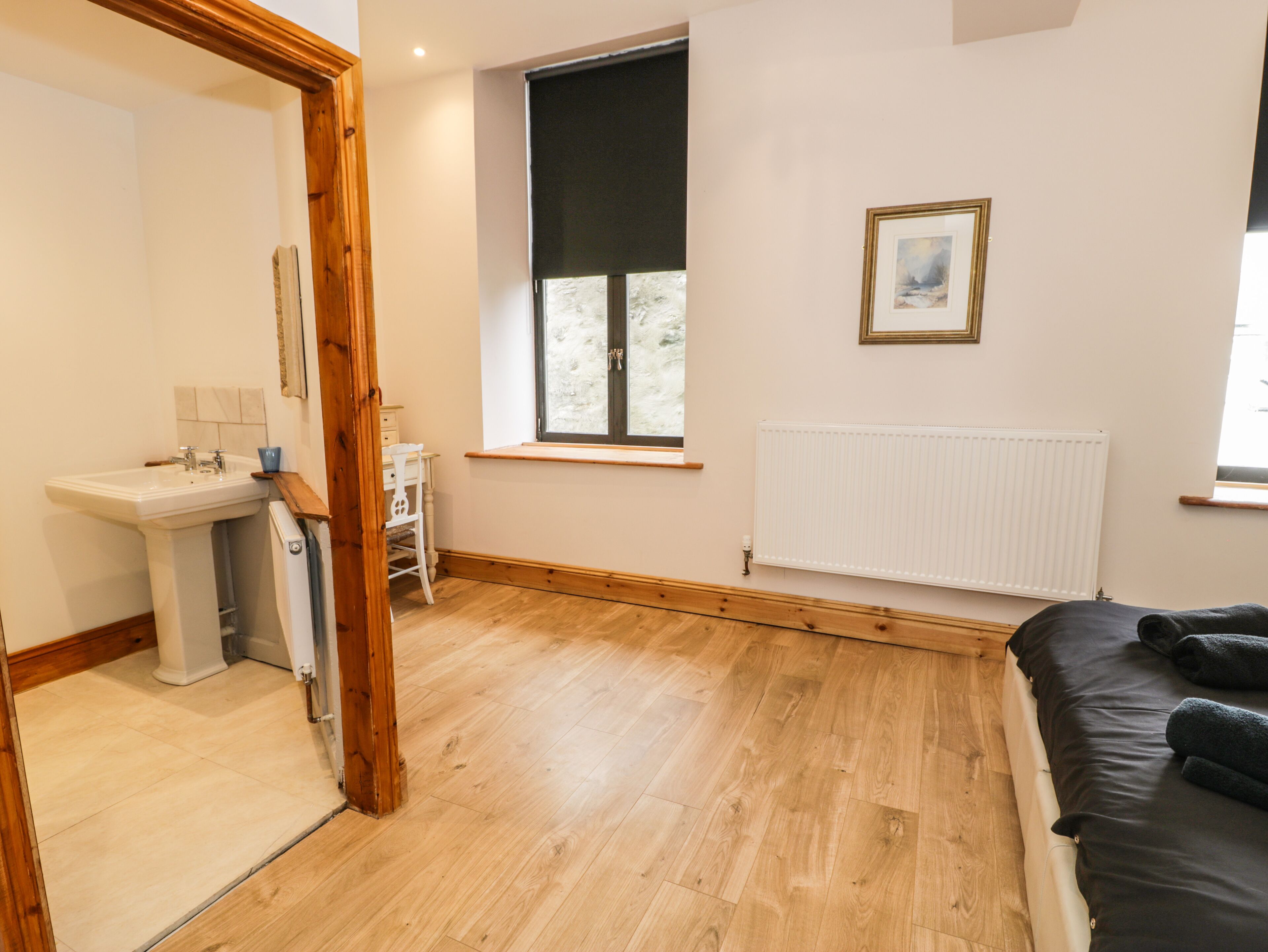 A bedroom with a wooden floor, a window with a view, a radiator, and a bed with pillows.