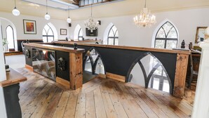A spacious room with wooden flooring, a large central bar area, and arched windows. - Greystones Chapel (Caernarfon)