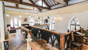 A spacious room with a wooden bar, arched windows, and a high ceiling with exposed beams. - Greystones Chapel (Caernarfon)