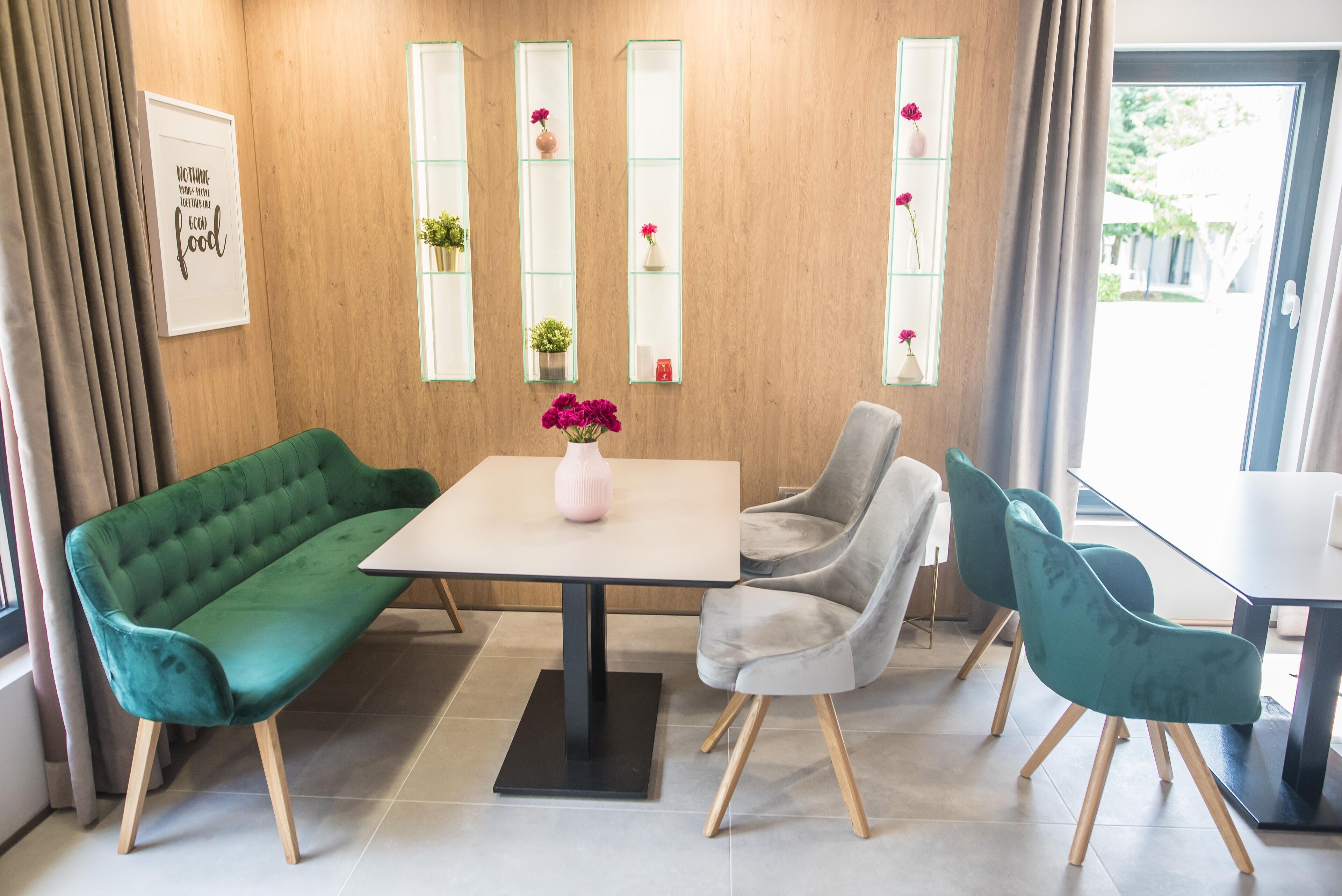 A modern dining area with a green sofa, grey chairs, and a table with a vase of flowers.