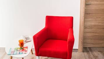 A red armchair, a small table with a magazine, a phone, and a candle, against a white wall with a flat-screen TV above.
