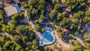 Vista aérea de un complejo turístico con una piscina central, rodeado de exuberante vegetación y varias edificaciones.