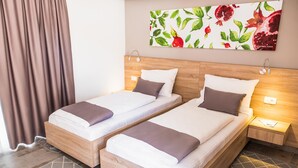 Habitación de hotel con dos camas individuales, cabecero de madera, mesita de noche con lámpara y una obra de arte con motivos de granada en la pared.